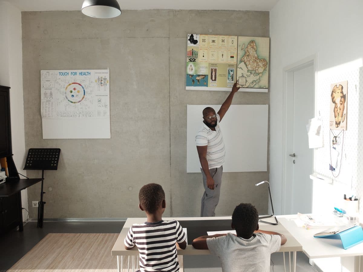 A tutor leaning over a desk to explain a lesson to two students