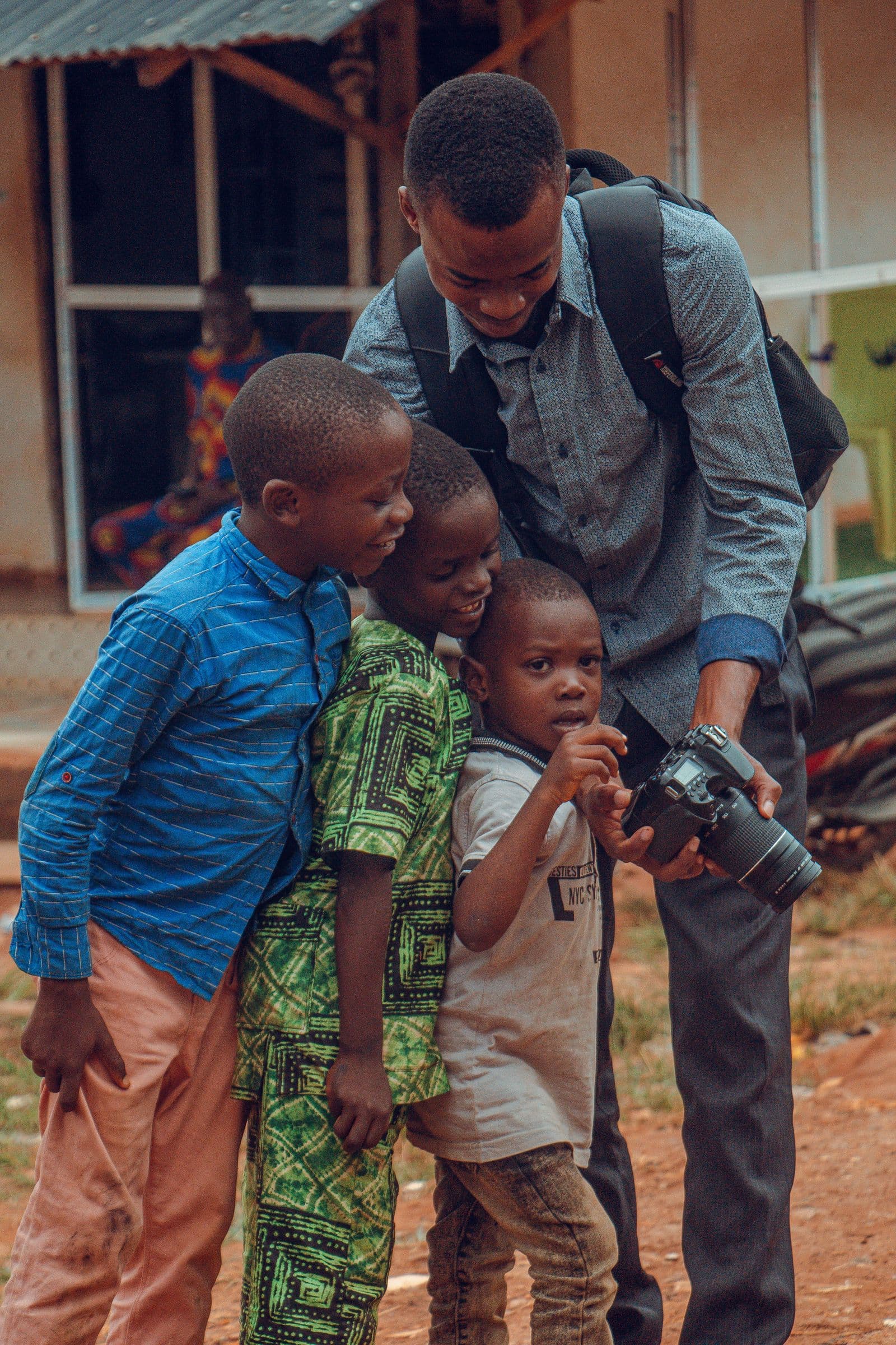 A man showing three boys the screen of his camera outdoors