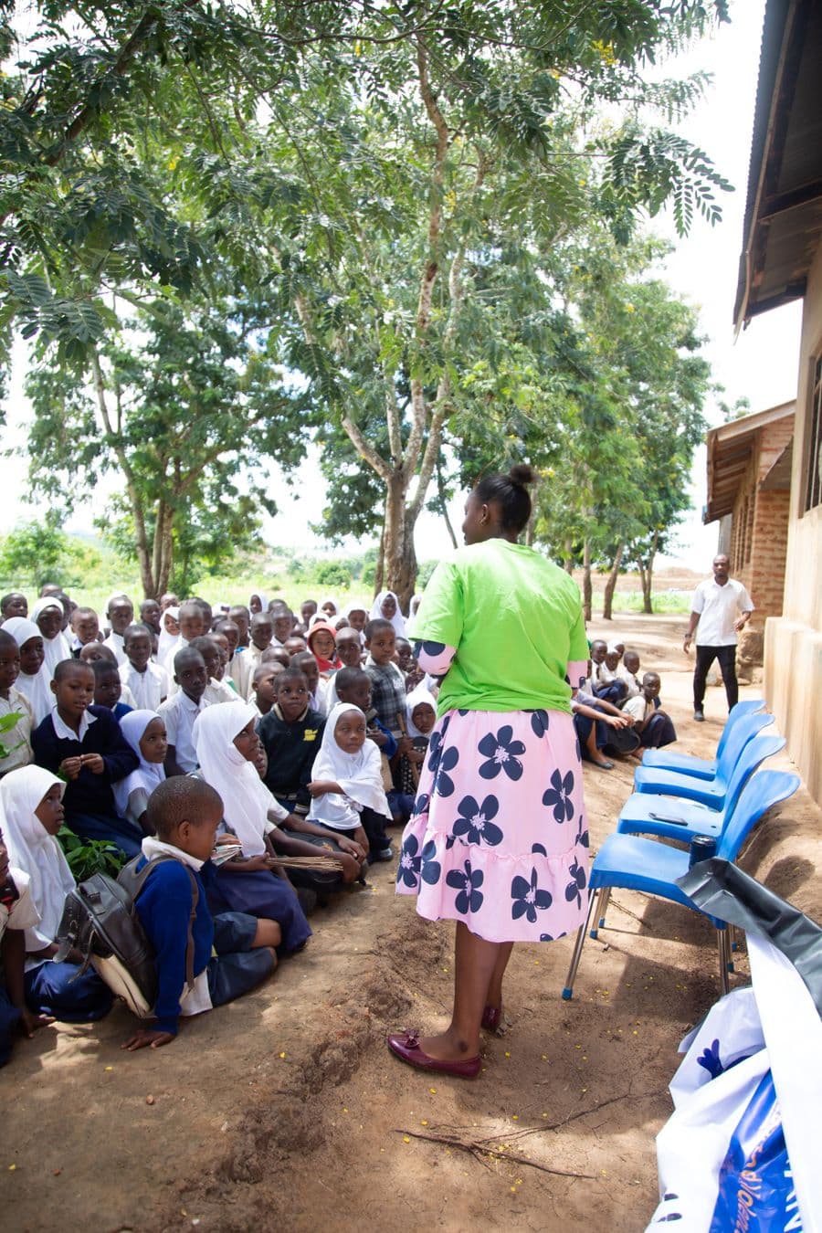 A teacher leading an outdoor lesson with children seated under trees